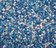 A close-up view of a textured surface covered in small blue, white, and light blue rubber granules mixed together.