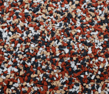 Close-up of a surface covered with small, irregularly shaped granules in red, black, white, and tan colors, creating a speckled, textured pattern.