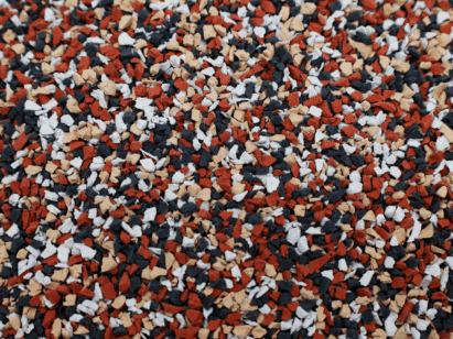 Close-up of a surface covered with small, irregularly shaped granules in red, black, white, and tan colors, creating a speckled, textured pattern.