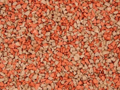 A close-up view of small, irregularly shaped granules in shades of orange and beige, resembling gravel or crushed stone, densely packed together.