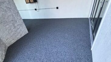 A clean, empty room with light gray speckled flooring, white walls, a window, a glass door, and visible electrical outlets and wiring on one wall.