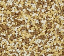 A close-up of a surface covered in small, irregularly shaped tan, brown, and white chips, resembling decorative gravel or textured flooring material.