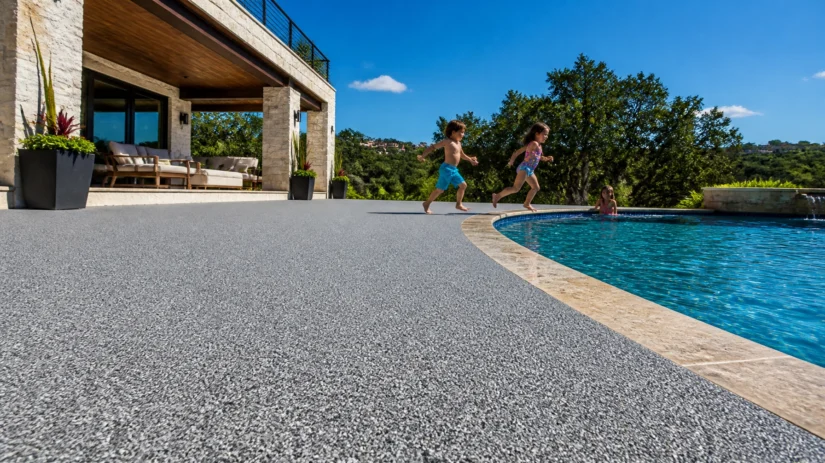 sJeYUmNlB5F Three children run toward a backyard pool on a sunny day beside a modern house, while another child sits at the pool’s edge. Trees and blue sky are in the background.