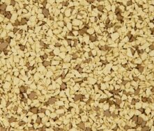 A close-up of a textured surface covered with small, irregularly shaped beige and light brown granules, resembling instant coffee or cereal flakes.